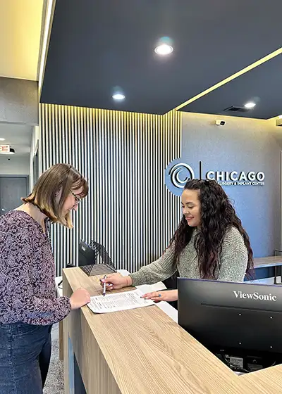 A receptionist at Chicago Oral Surgery and Implant Center helping a patient fill out a form.