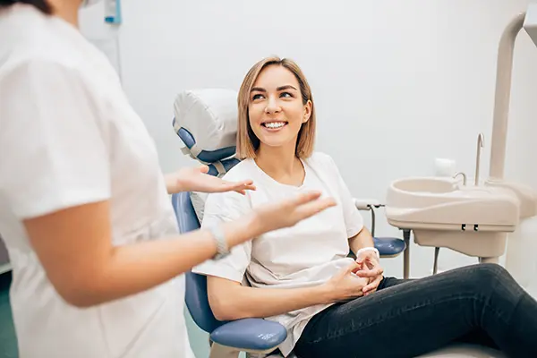 Smiling patient calmly sitting a dental chair while her dental assistant speaks with her